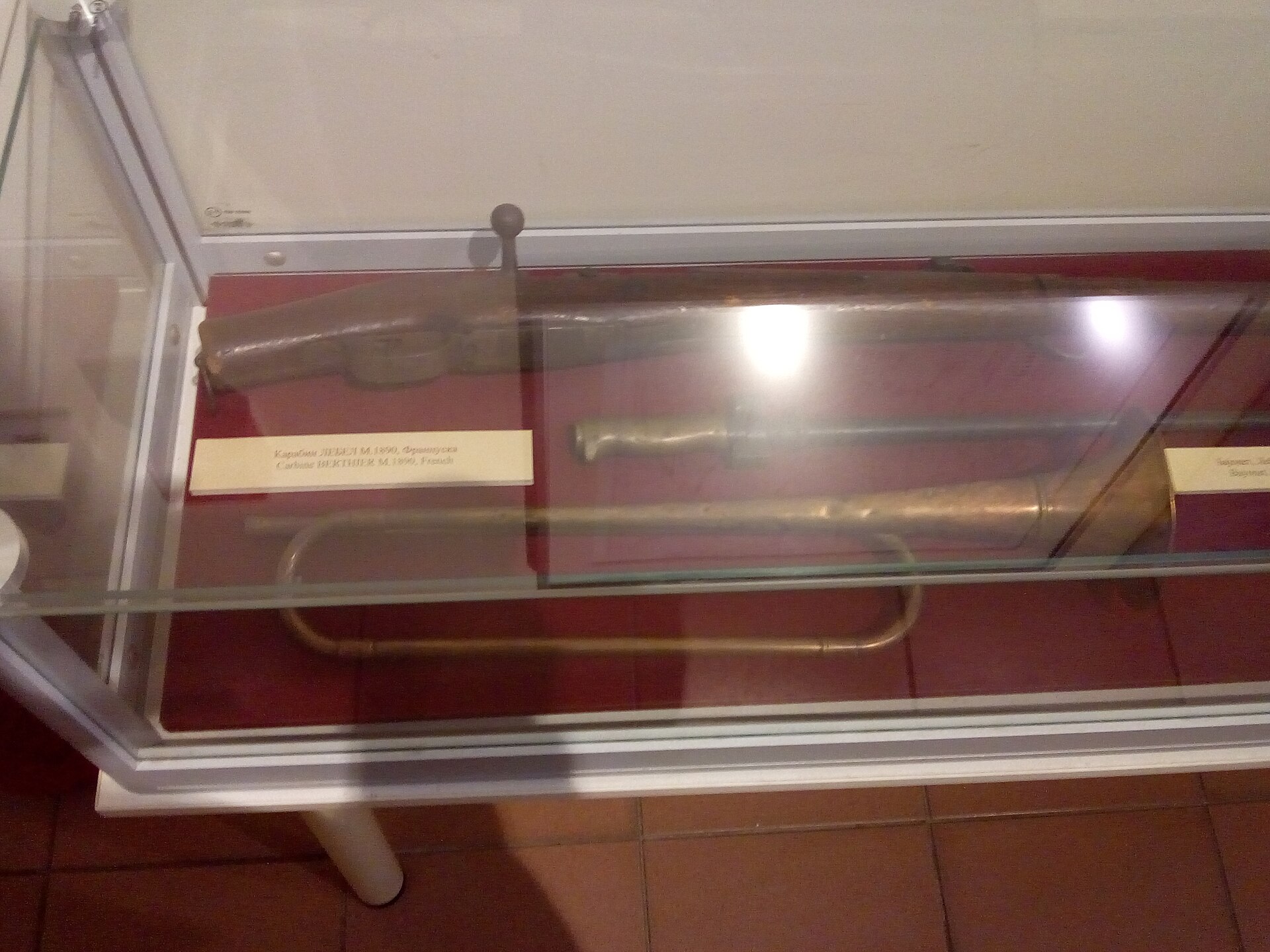 Glass case with an old cannon barrel and metal artifacts on red backing