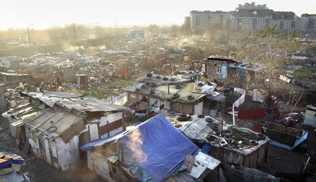 Cluster of makeshift huts with tarps and debris near apartment blocks in Belgrade