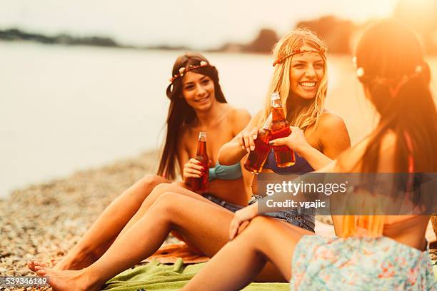 Friends sitting on the lakeside shore at Ada Ciganlija, holding drinks in warm sunlight