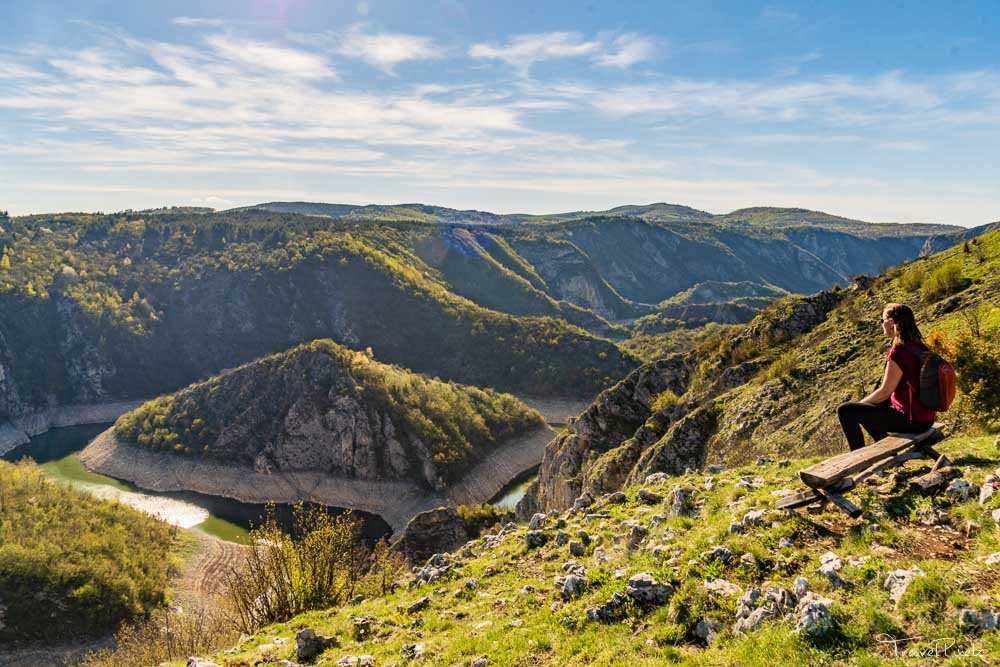 Hiker seated on a bench overlooking winding Uvac Canyon cliffs and river bend