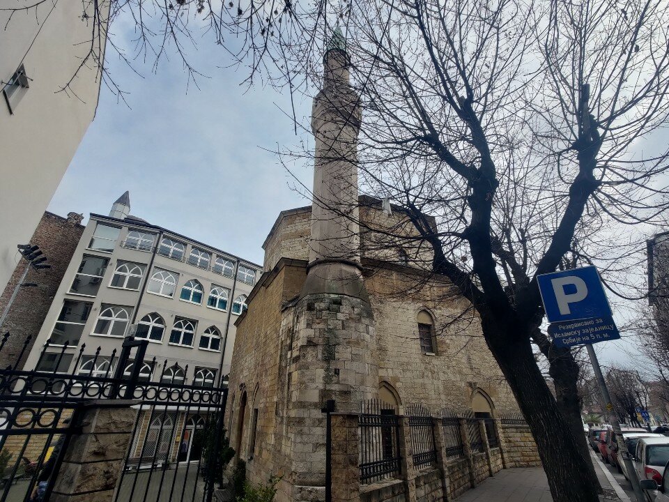 Stone mosque with a tall minaret beside a street, framed by bare trees in Bajrakli Mosque, Belgrade