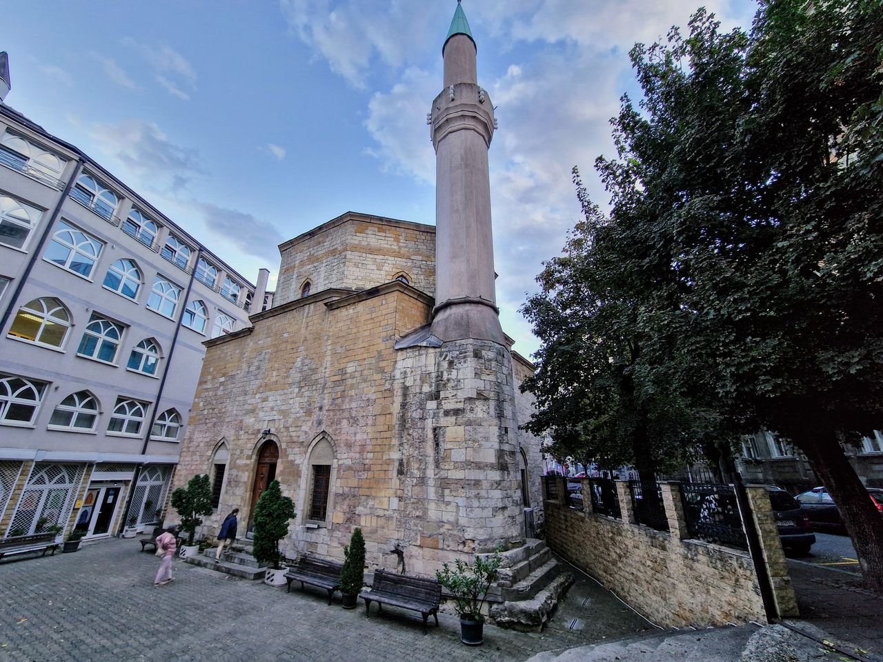 Stone Bajrakli Mosque with tall minaret beside modern buildings in Belgrade courtyard