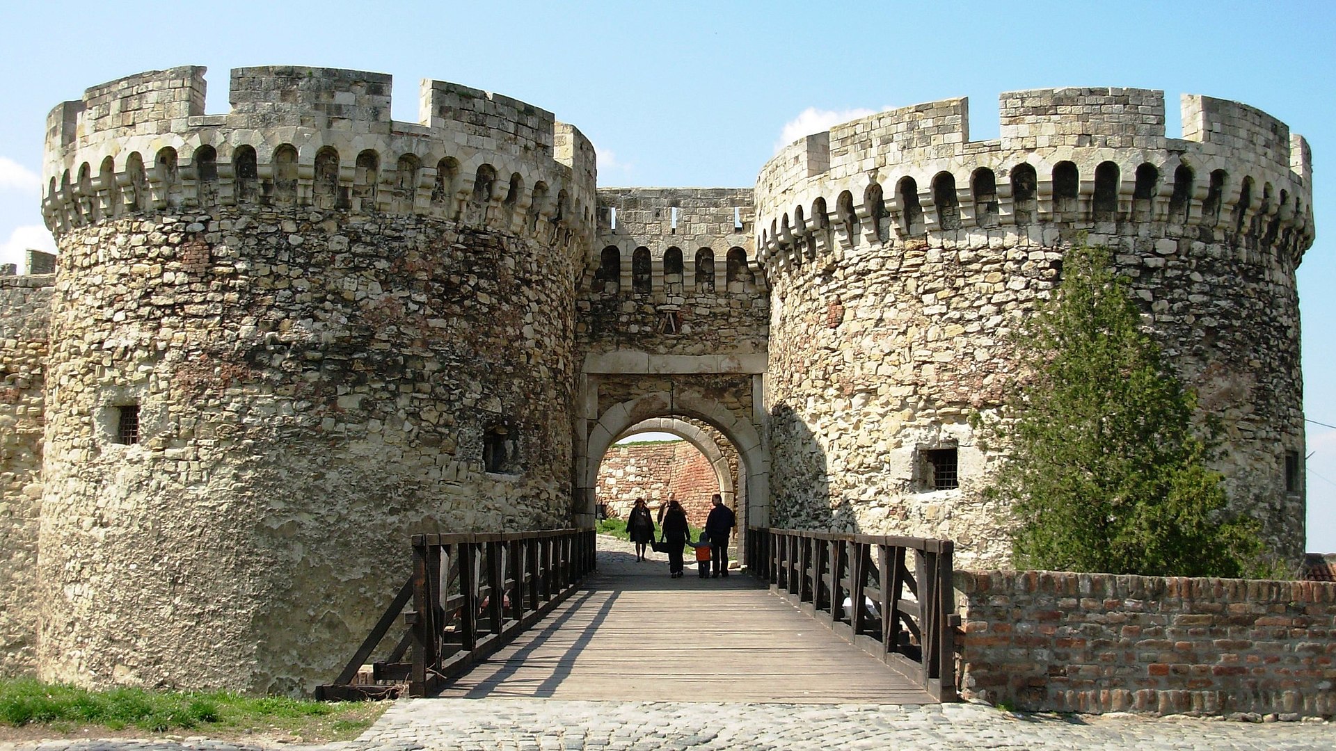 Medieval stone gate with round towers and a wooden bridge at Belgrade Waterfront