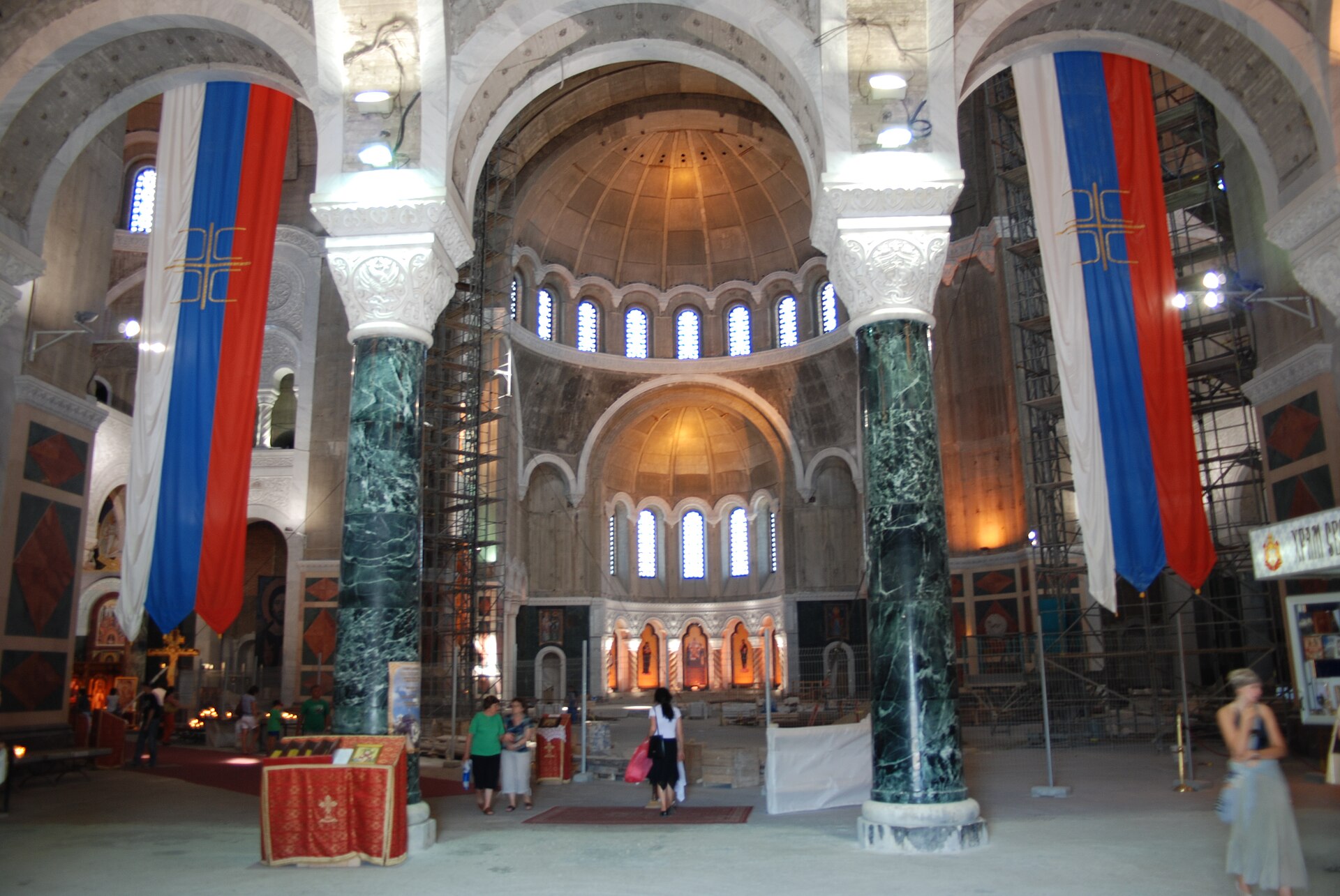 Interior of Cathedral of Saint Sava in Belgrade with arches, marble columns, and hanging Serbian flags