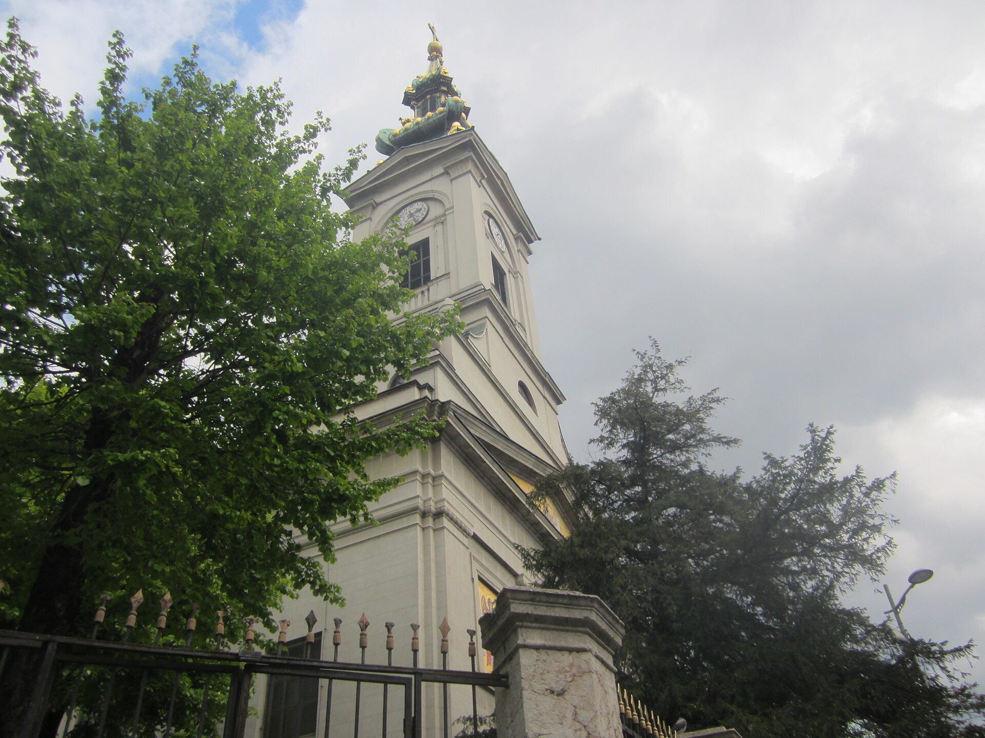 Clock tower of the Cathedral of St. Michael rises above trees and a fence in Belgrade