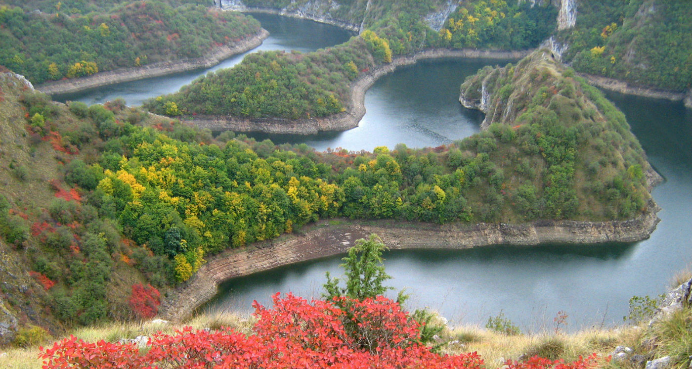 Curving river bends through wooded cliffs with autumn colors near Deliblato Sands