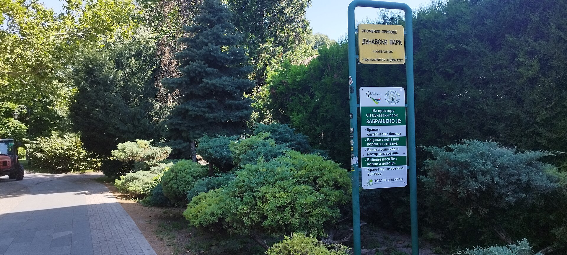 Park path beside a regulation sign in Dunavski Park, Novi Sad, surrounded by dense trees