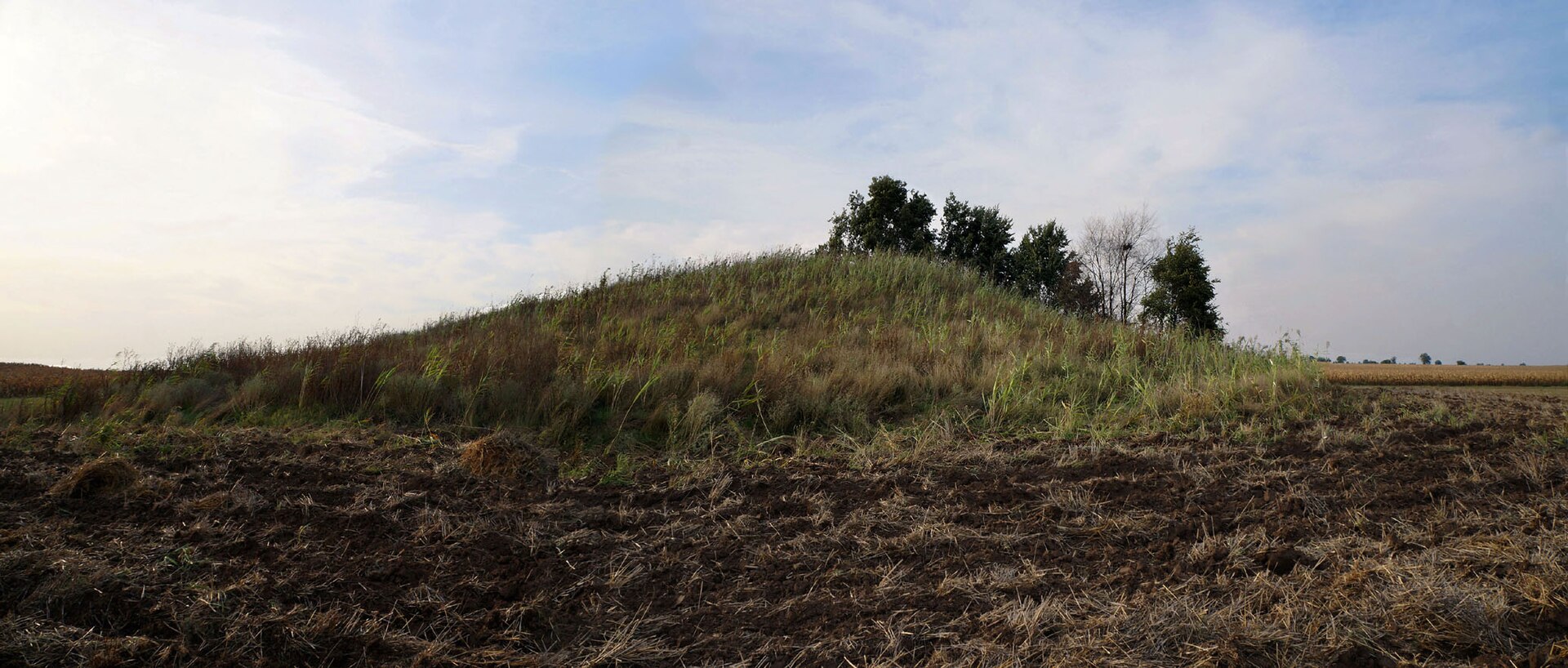 Low grassy mound rising above harvested fields in Eastern Serbia under a pale sky