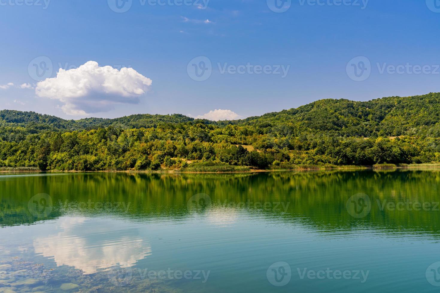 Calm lake reflecting clouds, with forested hills in Eastern Serbia under a blue sky
