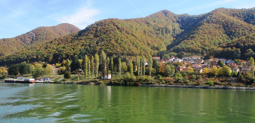 Riverside village beneath forested hills, with green water in Eastern Serbia