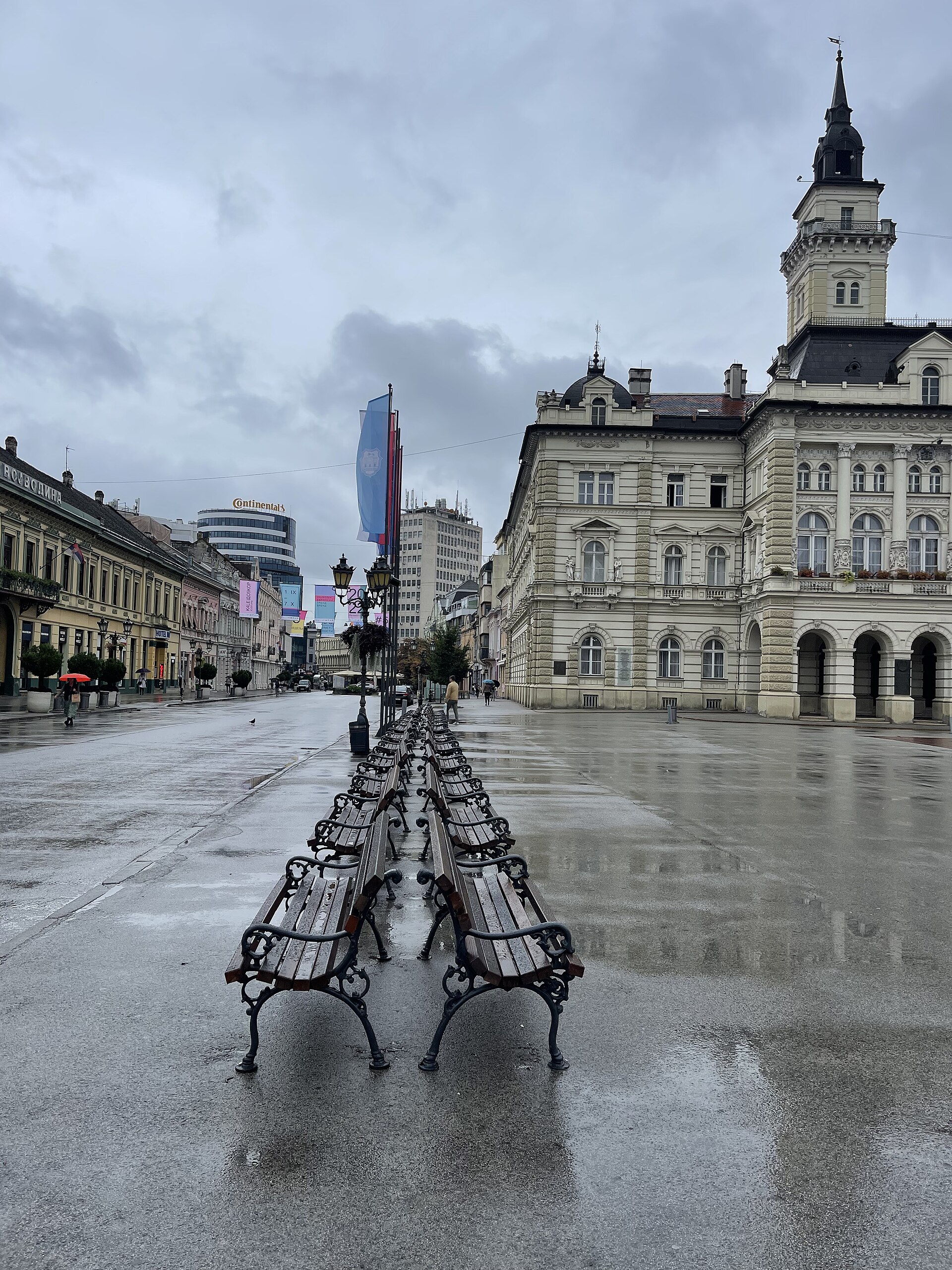 Wet benches on Freedom Square in Novi Sad with historic buildings and a tall tower nearby