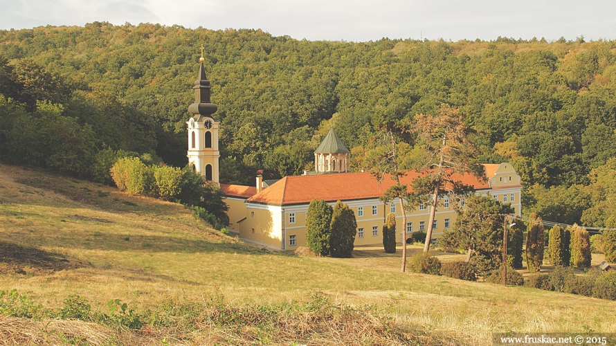 Monastery complex with bell tower on a grassy hillside in Fruska Gora, backed by dense forest