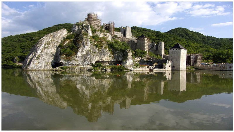 Golubac Fortress on a rocky cliff above the Danube with walls reflected in calm water