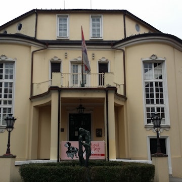 Historic building facade with a central balcony, flag, and statue at Imperial Palace of Sirmium