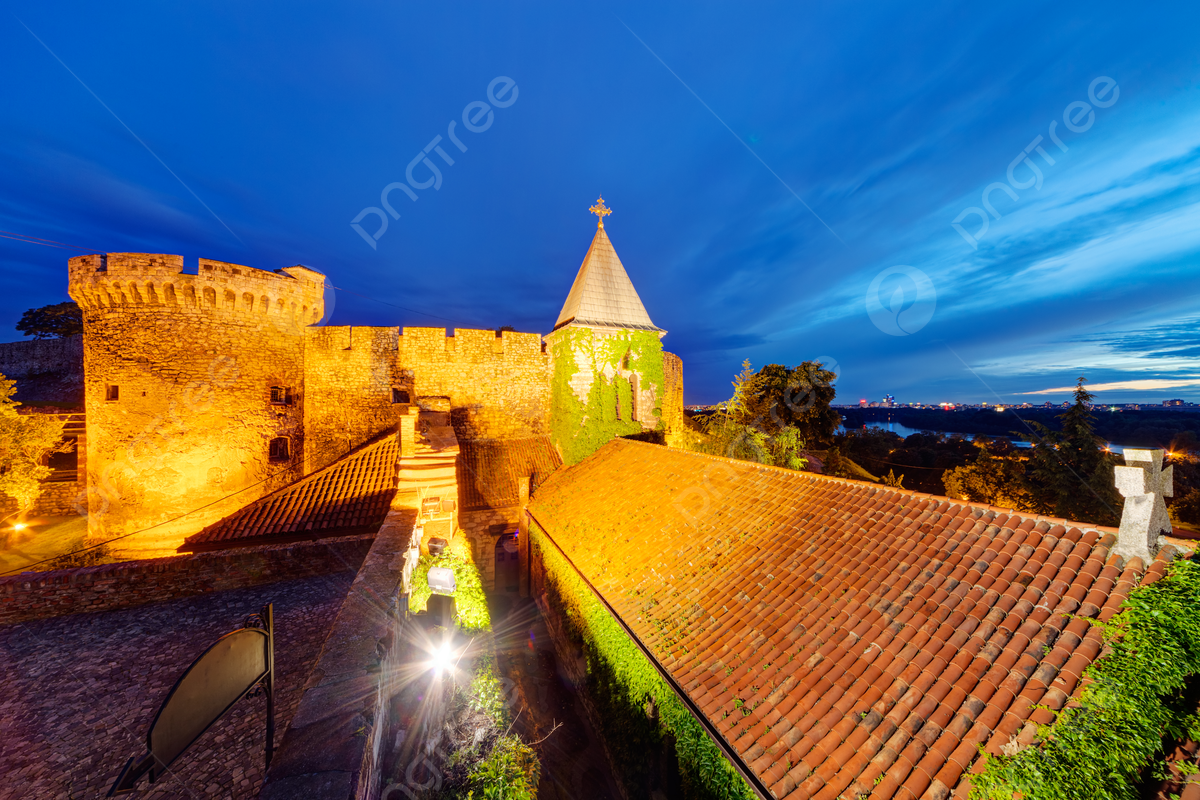 Illuminated stone fortress walls and a conical tower above tiled rooftops at Kalemegdan Park in Belgrade