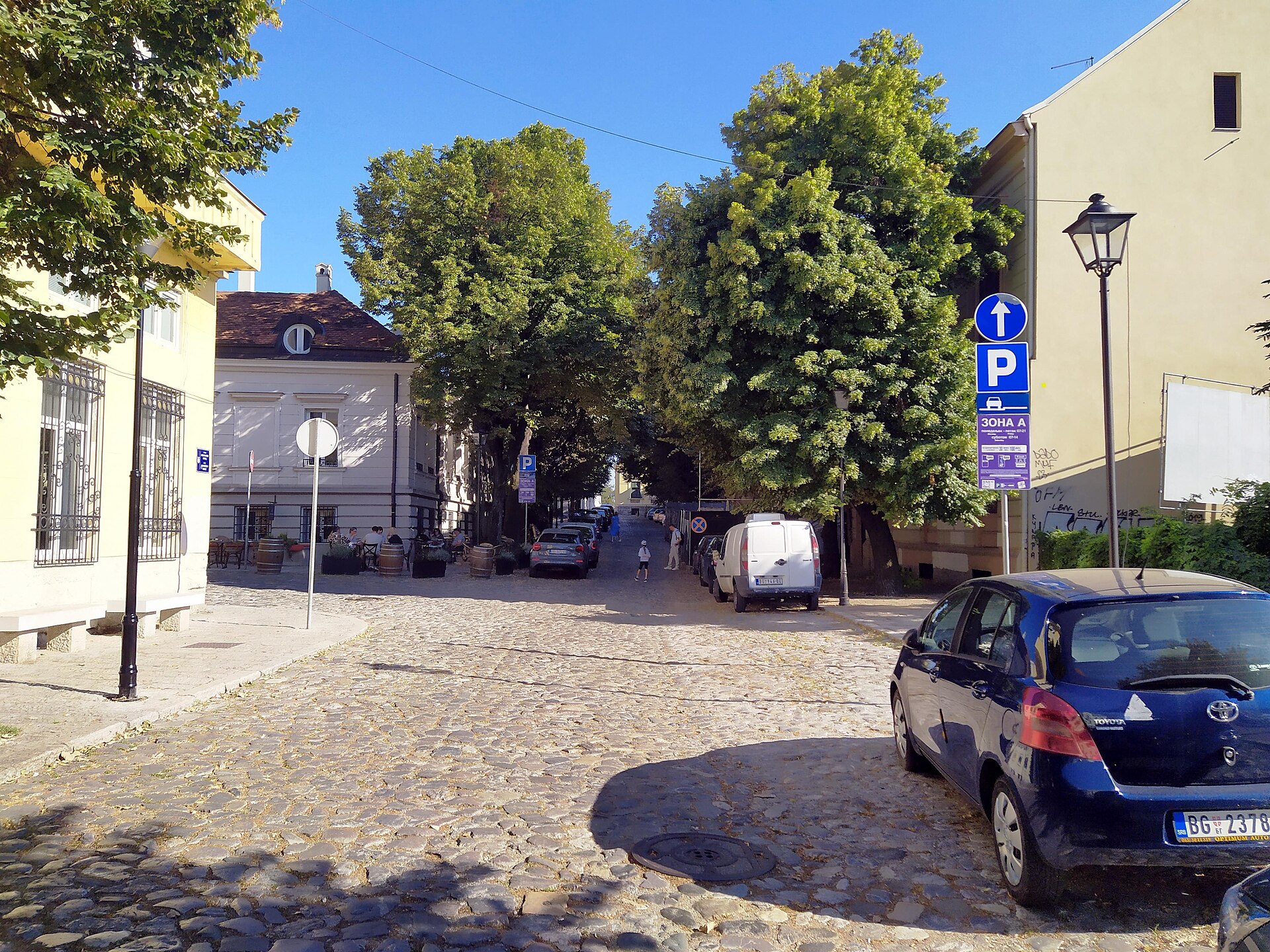 Cobblestone street with trees, parked cars, and low buildings in Kosančićev Venac, Belgrade