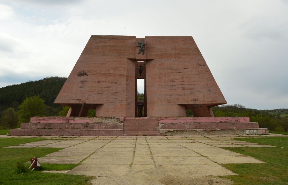 Large concrete memorial on a stepped platform in Kragujevac with hills and open sky behind it