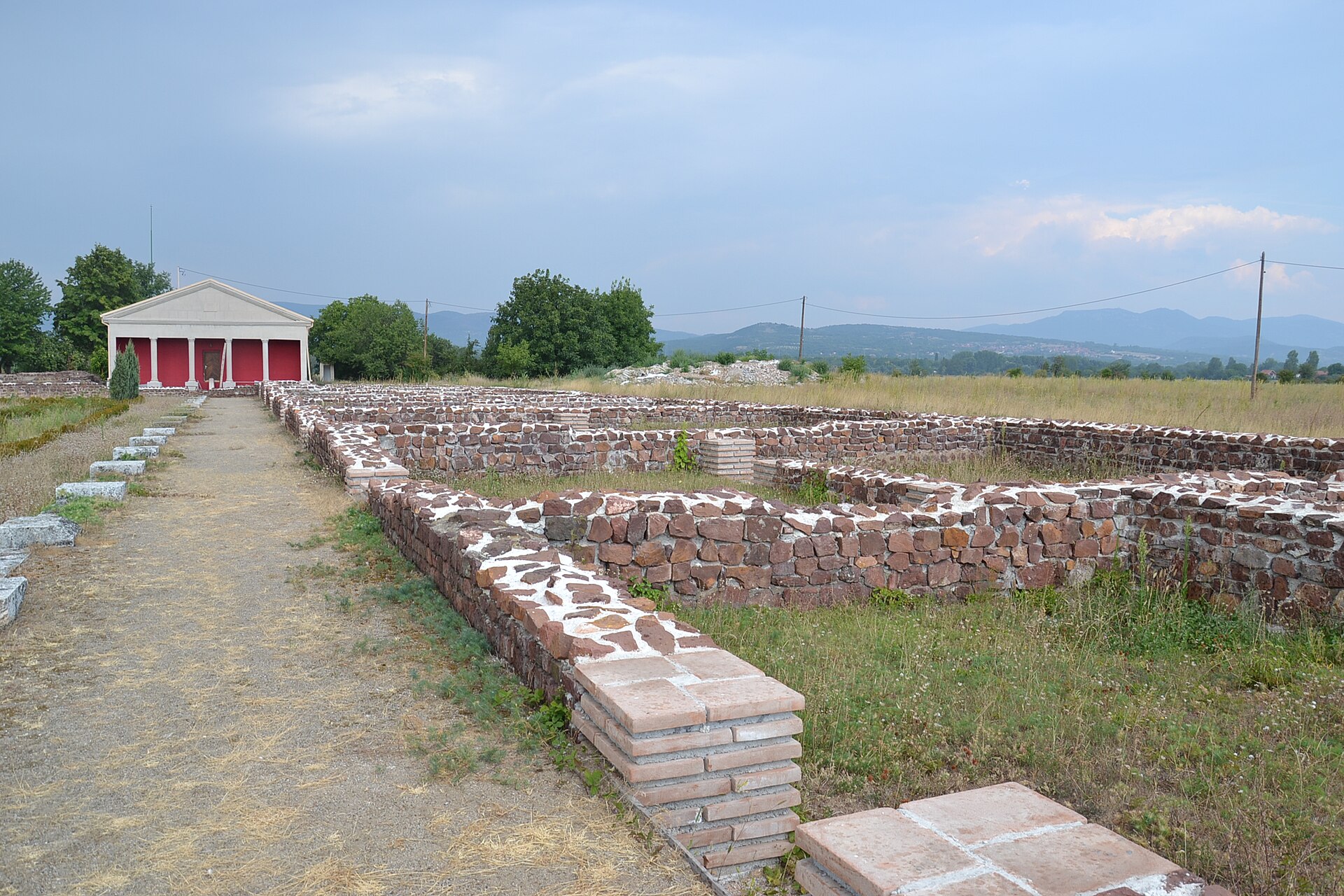 Stone ruin foundations and a small reconstructed pavilion at Mediana in Niš, with hills beyond