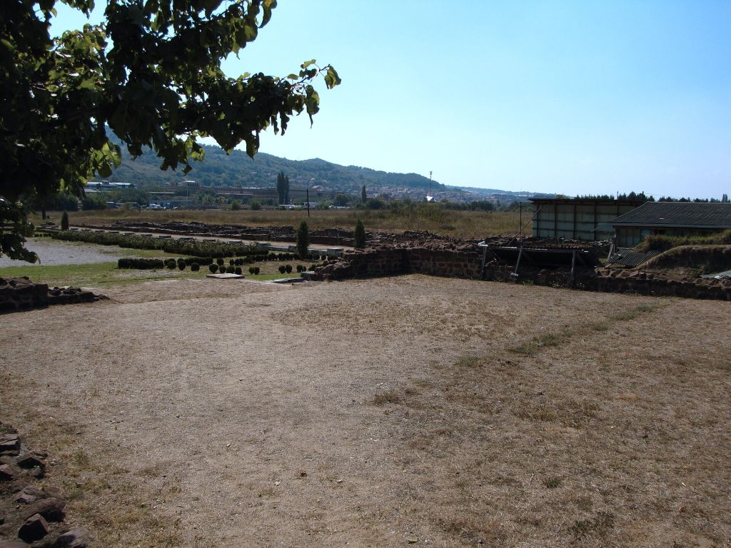 Stone ruins and open grassy ground at Mediana near Niš with distant hills and a clear sky