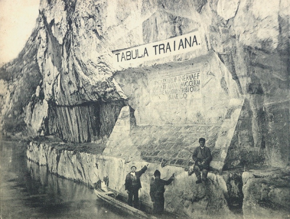 Tabula Traiana inscription carved into a Danube River cliff, with people and a boat below