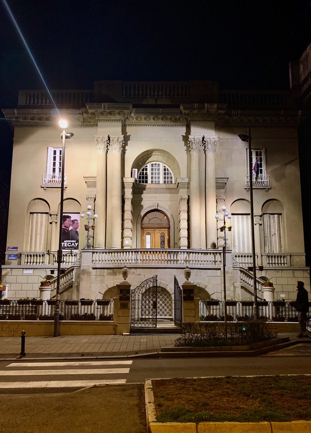 Night facade of the Nikola Tesla Museum in Belgrade with columns, arches, and a lit entrance