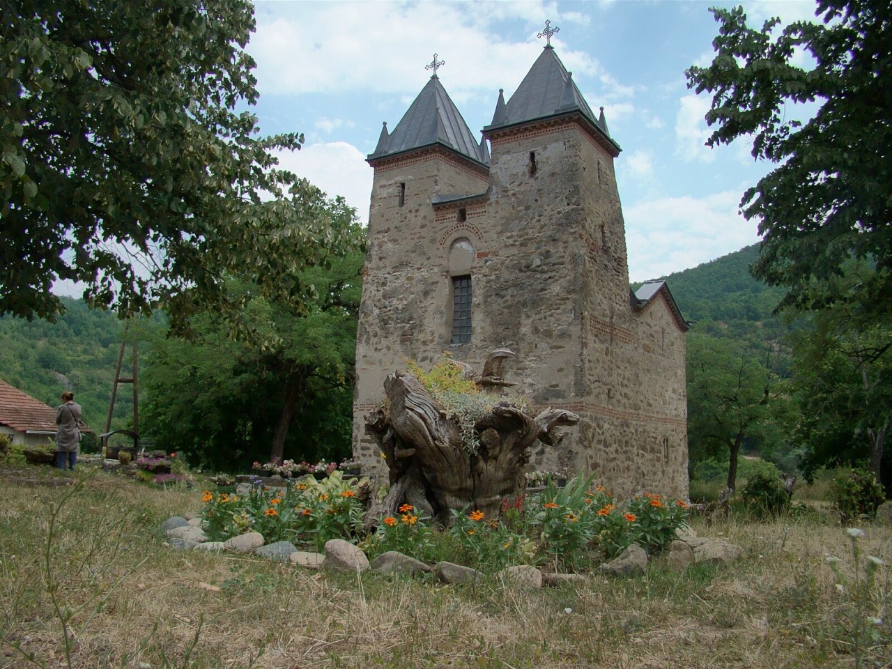 Small stone church with twin towers and cross finials in a wooded mountain setting