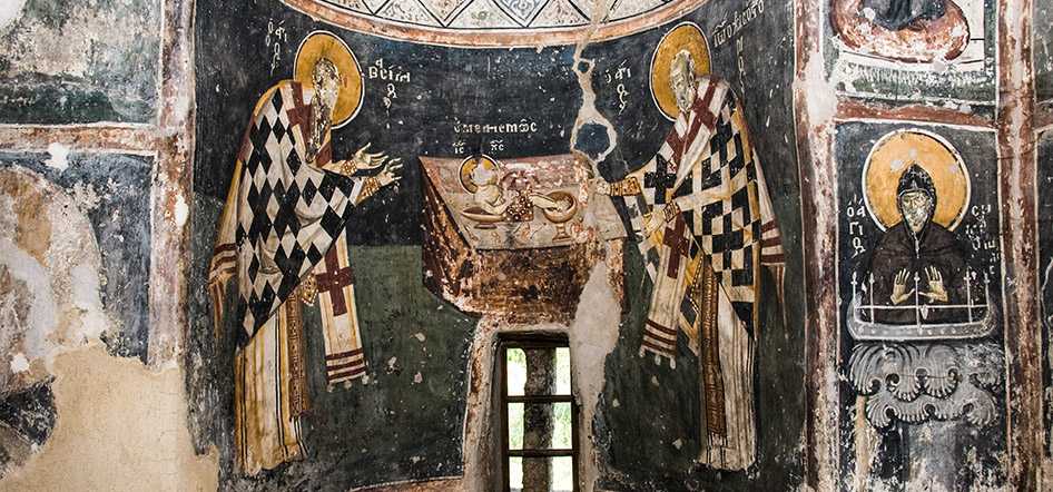 Two haloed saints painted on an aged church wall beside a small altar and narrow window