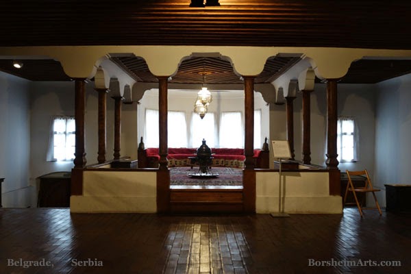 Historic sitting room with carved columns, rugs, and a chandelier inside Residence of Princess Ljubica in Belgrade