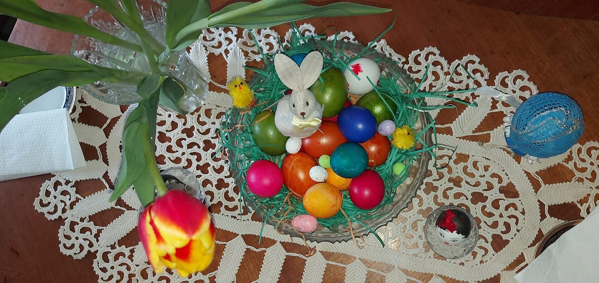 Colorful Easter eggs in a basket with a bunny, chicks, and lace table setting