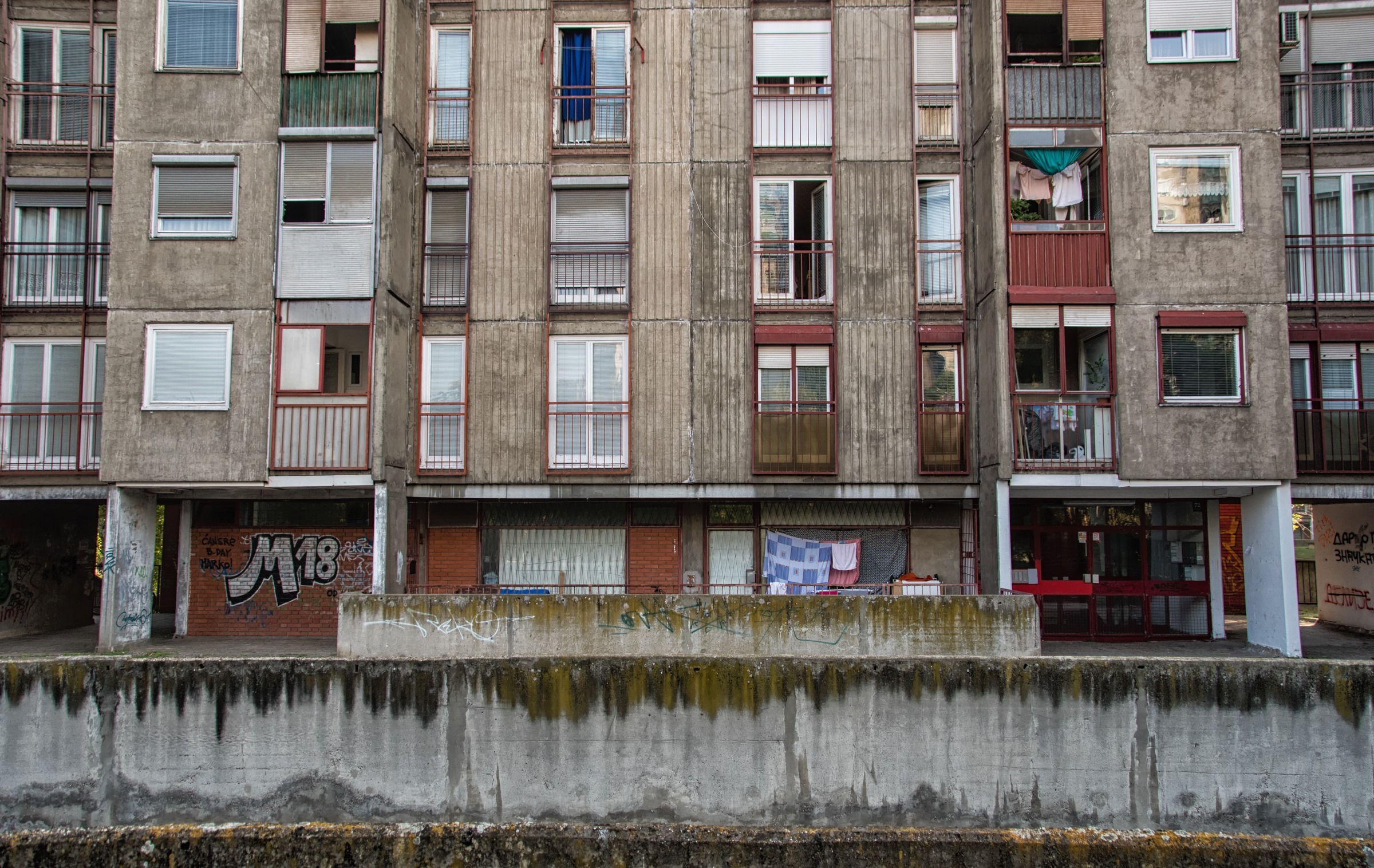Weathered apartment block beside a narrow concrete waterway, with graffiti and laundry on balconies