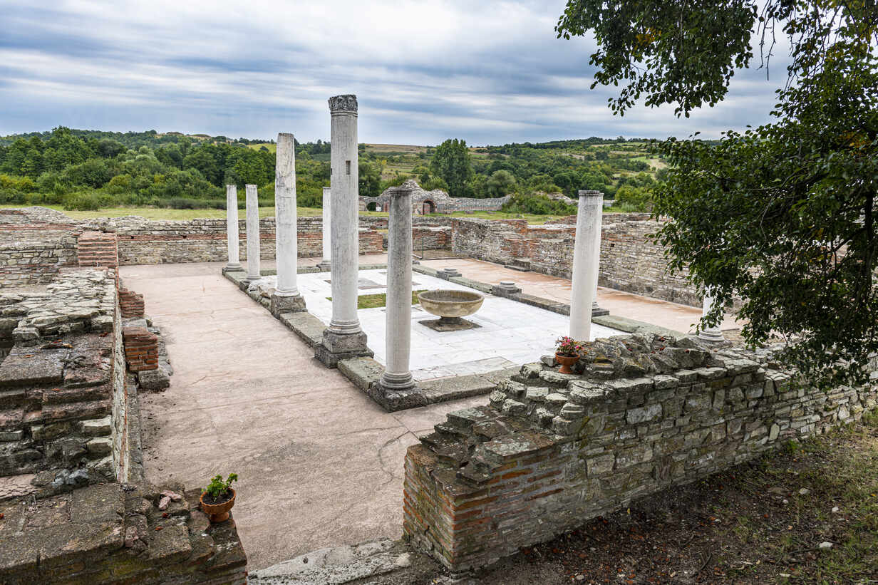 Ancient stone ruins with standing columns and low walls in a grassy Serbian landscape