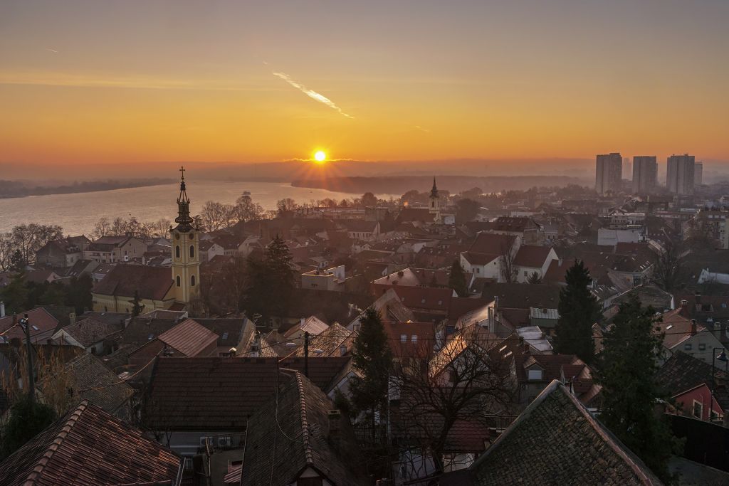 Sunset over rooftops, church towers, and a wide river in Serbia