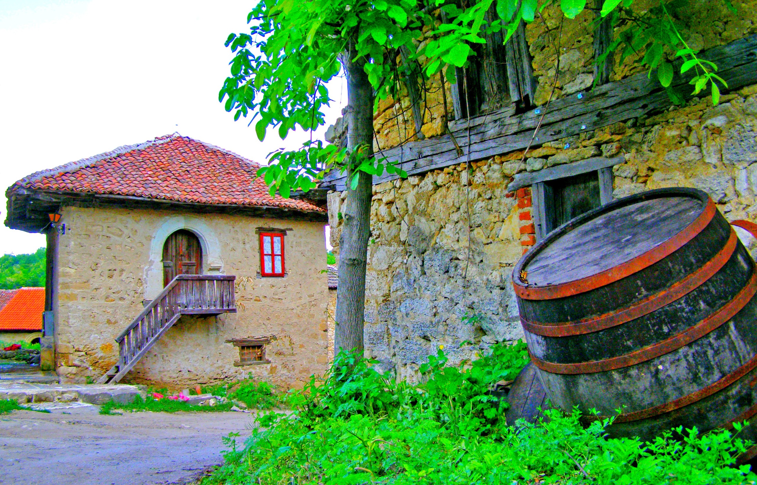 Stone wine cellar buildings with a large wooden barrel in a green courtyard