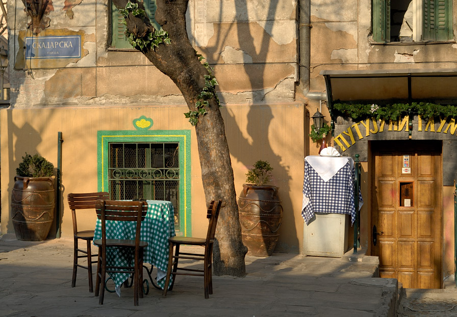 Outdoor restaurant tables beside a tree and wooden doorway in Skadarlija Bohemian Quarter, Belgrade