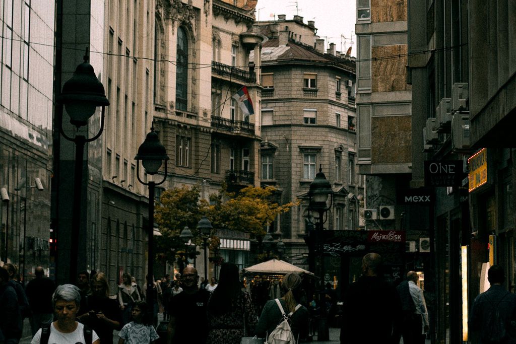Pedestrians walk along a narrow street lined with old buildings and lamps in Skadarlija Bohemian Quarter