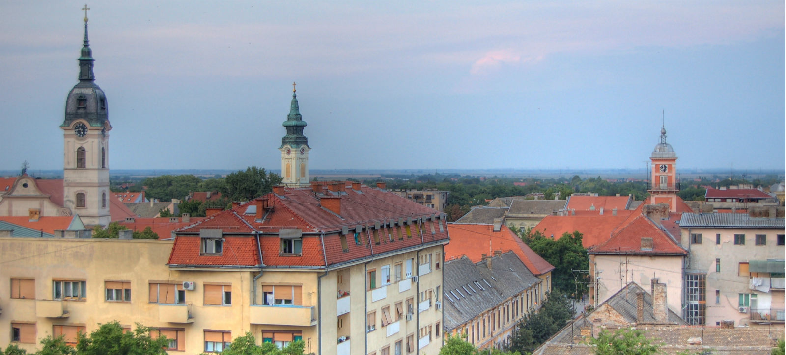 Church towers above red-roofed buildings in Sombor, with flat countryside on the horizon