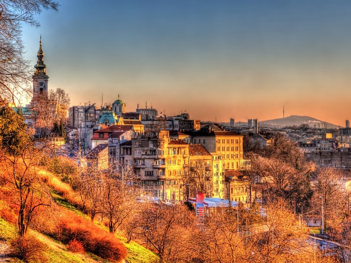 Sunset over Stari Grad Belgrade with church towers, dense rooftops, and a distant hill skyline