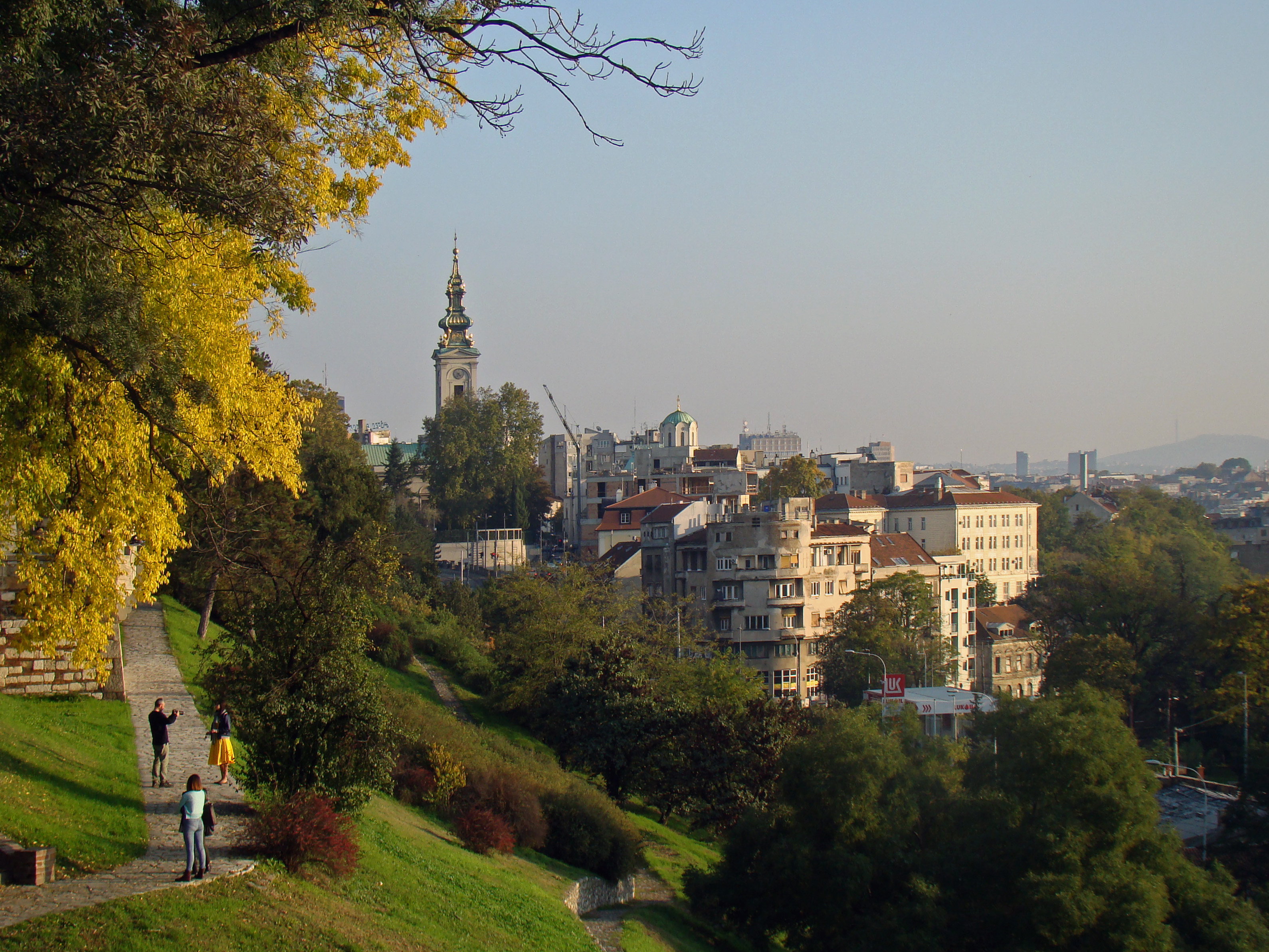 Stone path on a green hillside overlooking Belgrade rooftops and a church tower in Stari Grad