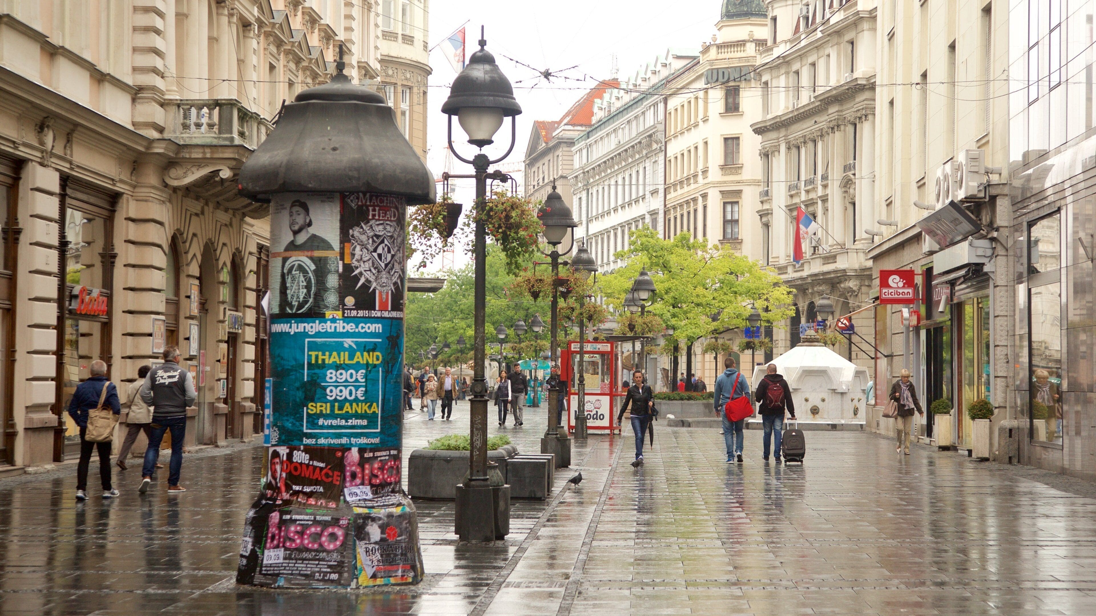 Rain-slick pedestrian street with historic buildings, lampposts, and walkers in Stari Grad, Belgrade