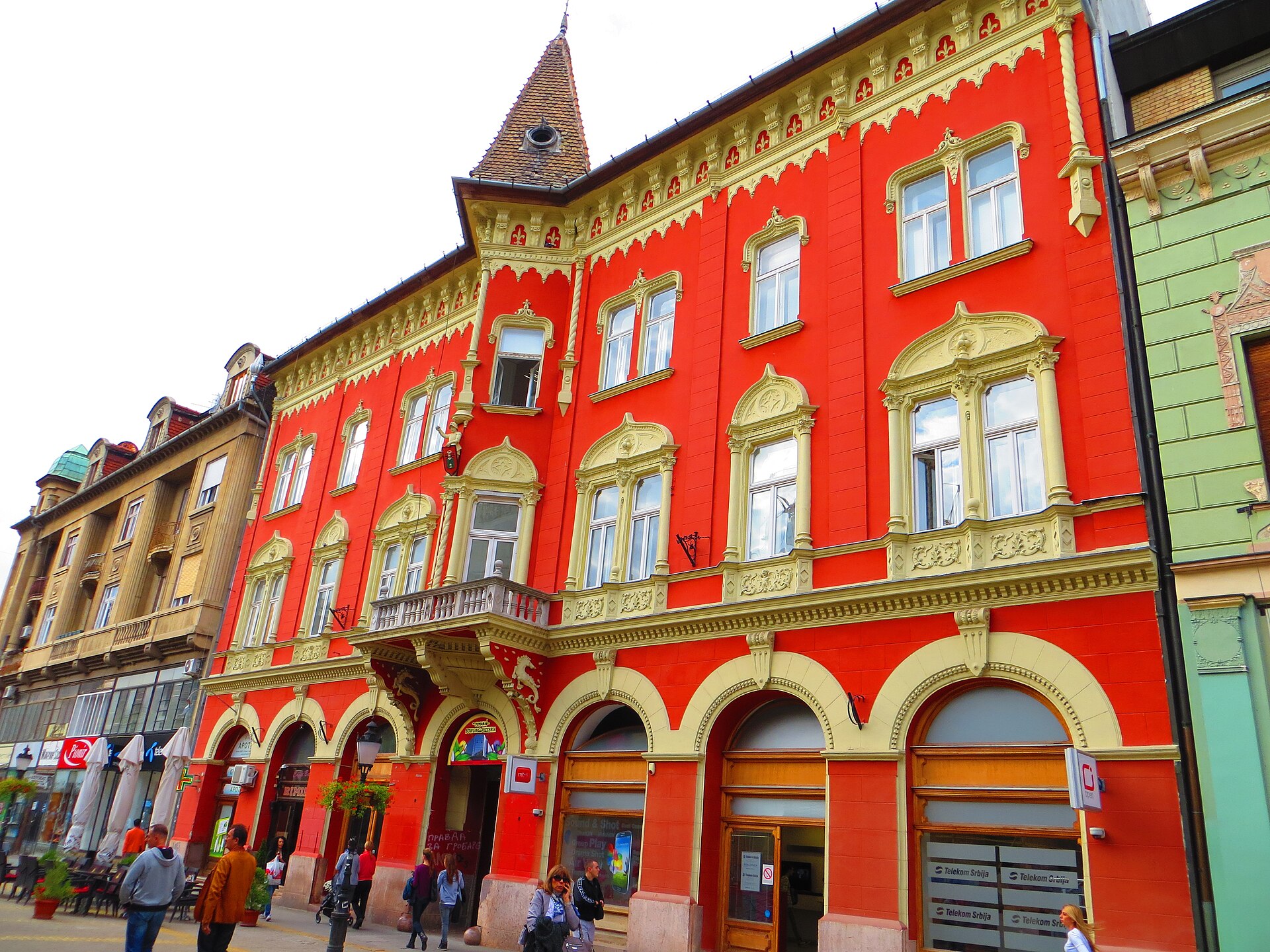 Ornate red historic building with cream trim and arched entrances in Subotica