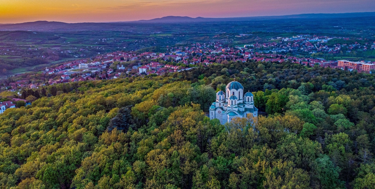 Domed church above dense forest with Topola spread across the hills in Šumadija