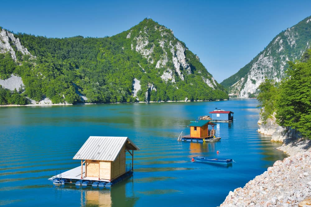 Floating cabins on a calm mountain lake beneath forested cliffs in Tara National Park