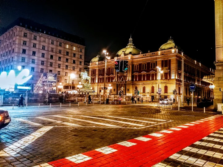 Illuminated historic buildings and wet paving at Trg Republike in Belgrade at night with a red walkway in front