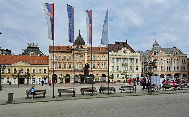 Historic façades on Liberty Square in Novi Sad with flags, benches, and a central statue