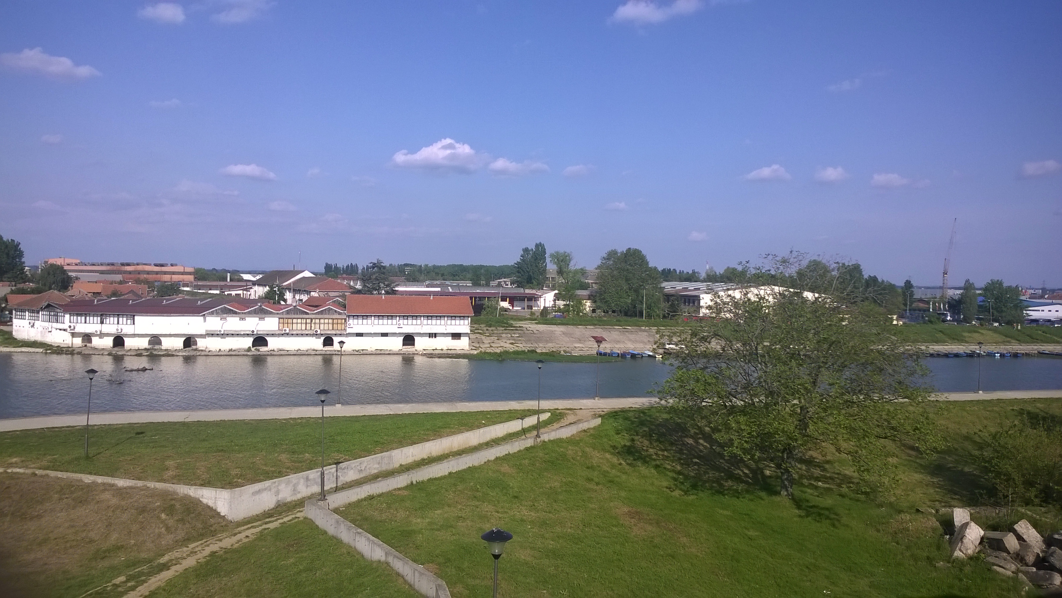 White riverside buildings beside a water channel, with grassy embankments and a clear sky in Smederevo