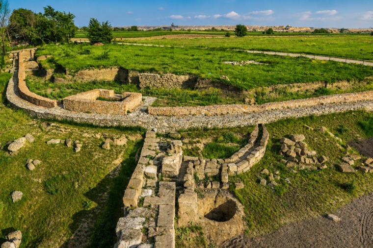 Curving stone foundations and grassy excavation areas at the Vinča Archaeological Site near Vinca