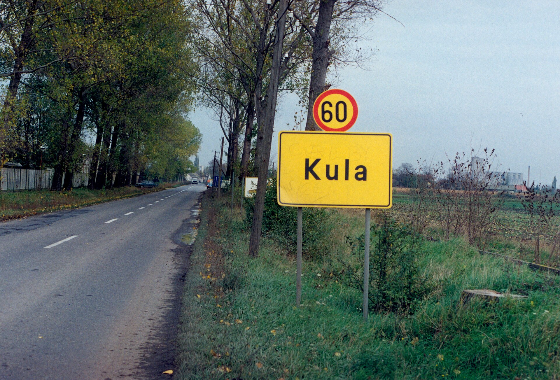 Road sign for Kula beside a rural road with trees and fields in Vojvodina