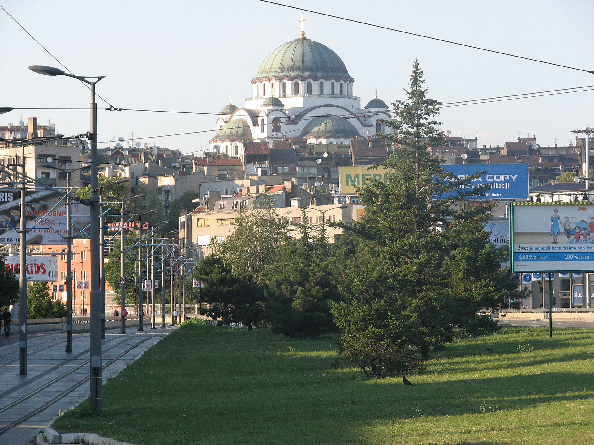 Temple of Saint Sava dome rising above Vračar streets with tram tracks, trees, and billboards