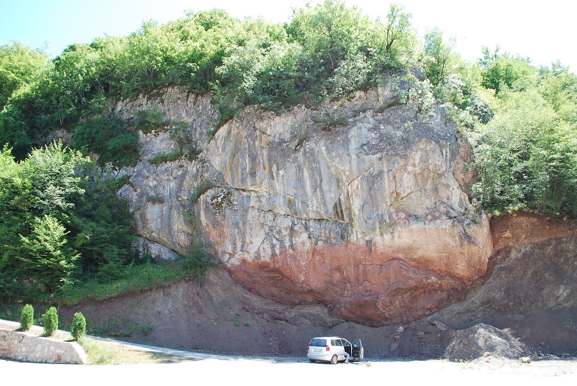 Layered rock cliff above a roadside clearing in Western Serbia, surrounded by dense forest