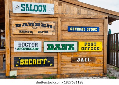 Wooden western-style facade with signs for saloon, barber, general store, doctor, bank, post office, sheriff, and jail